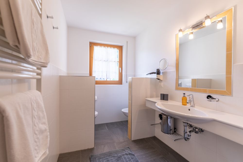 A bright, modern bathroom with a sink, mirror, and a separate area for the toilet and bidet.