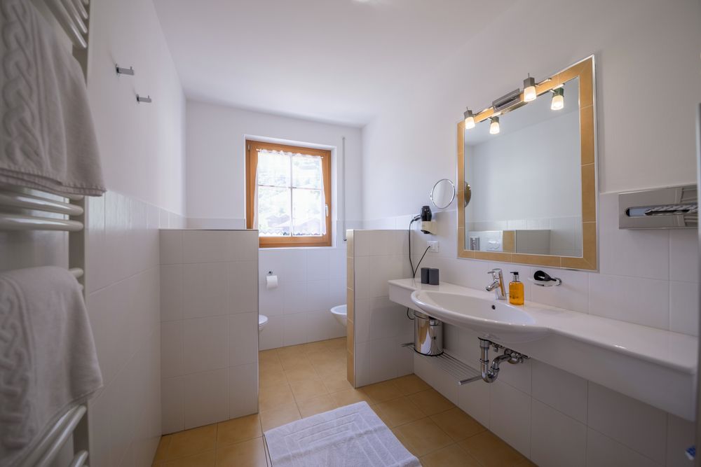 A bright, modern bathroom with a sink, a mirror, and a window in a separate area.