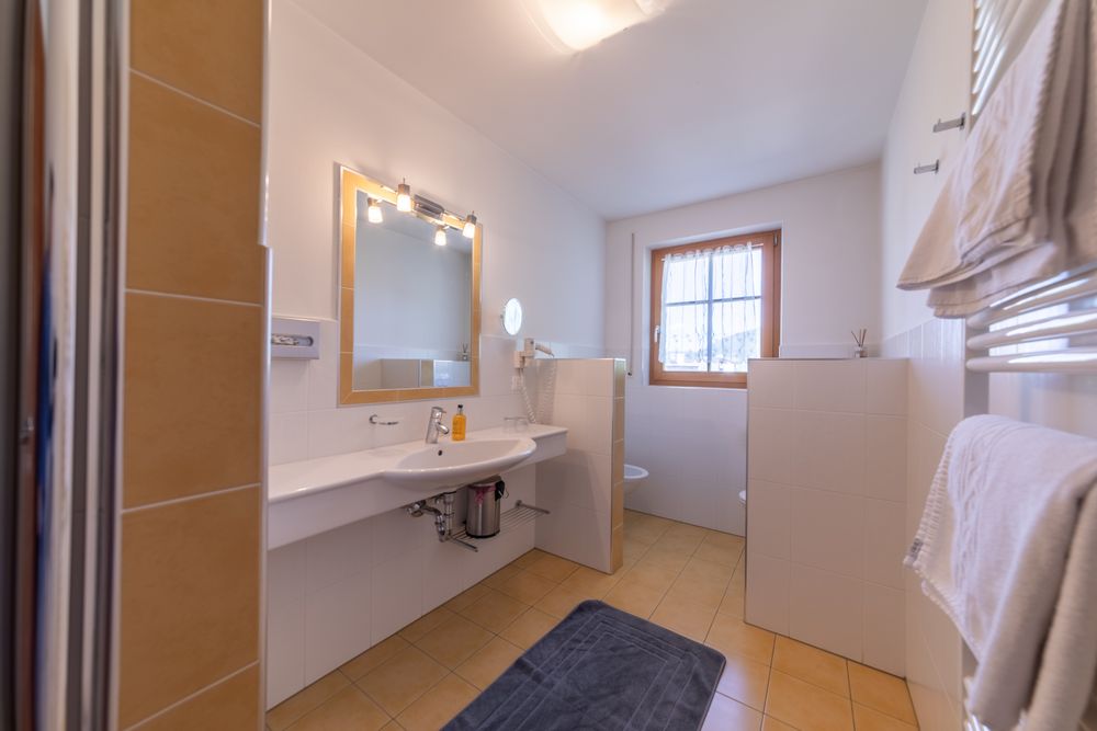 A bright, modern bathroom with a sink, mirror, towels, and tiled floor.