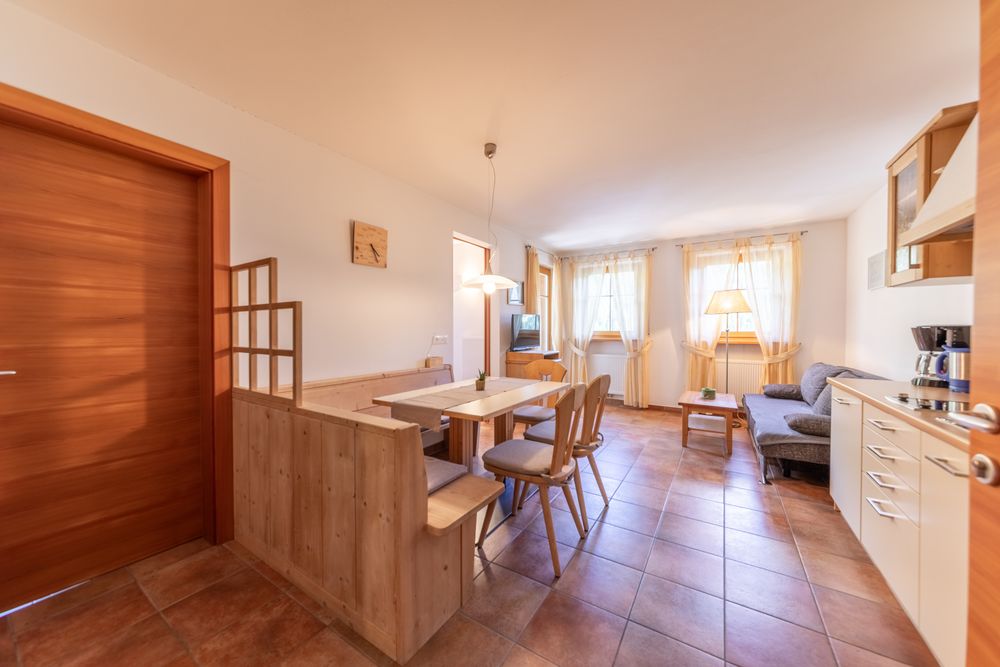 A cozy living and dining room with wooden furniture, tiled floor, a corner bench, and a kitchenette.