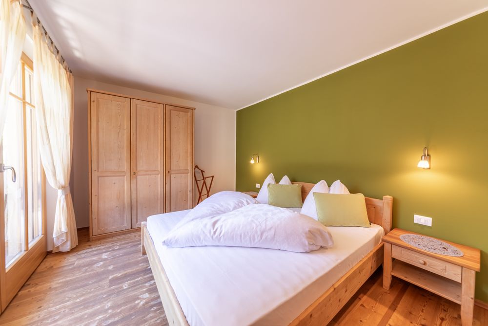 A cozy bedroom with a wooden double bed in front of a green wall and a matching wooden wardrobe.