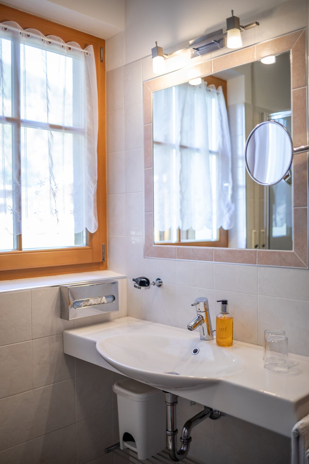 Ein weißes Badezimmerwaschbecken mit Spiegel, Fenster und flüssiger Seife.