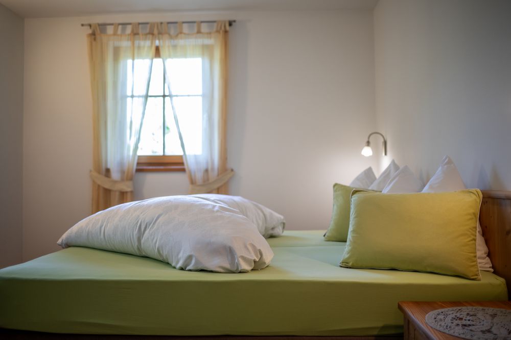 Ein gemütliches Schlafzimmer mit einem Doppelbett, hellgrüner Bettwäsche und einem Fenster mit Vorhängen.