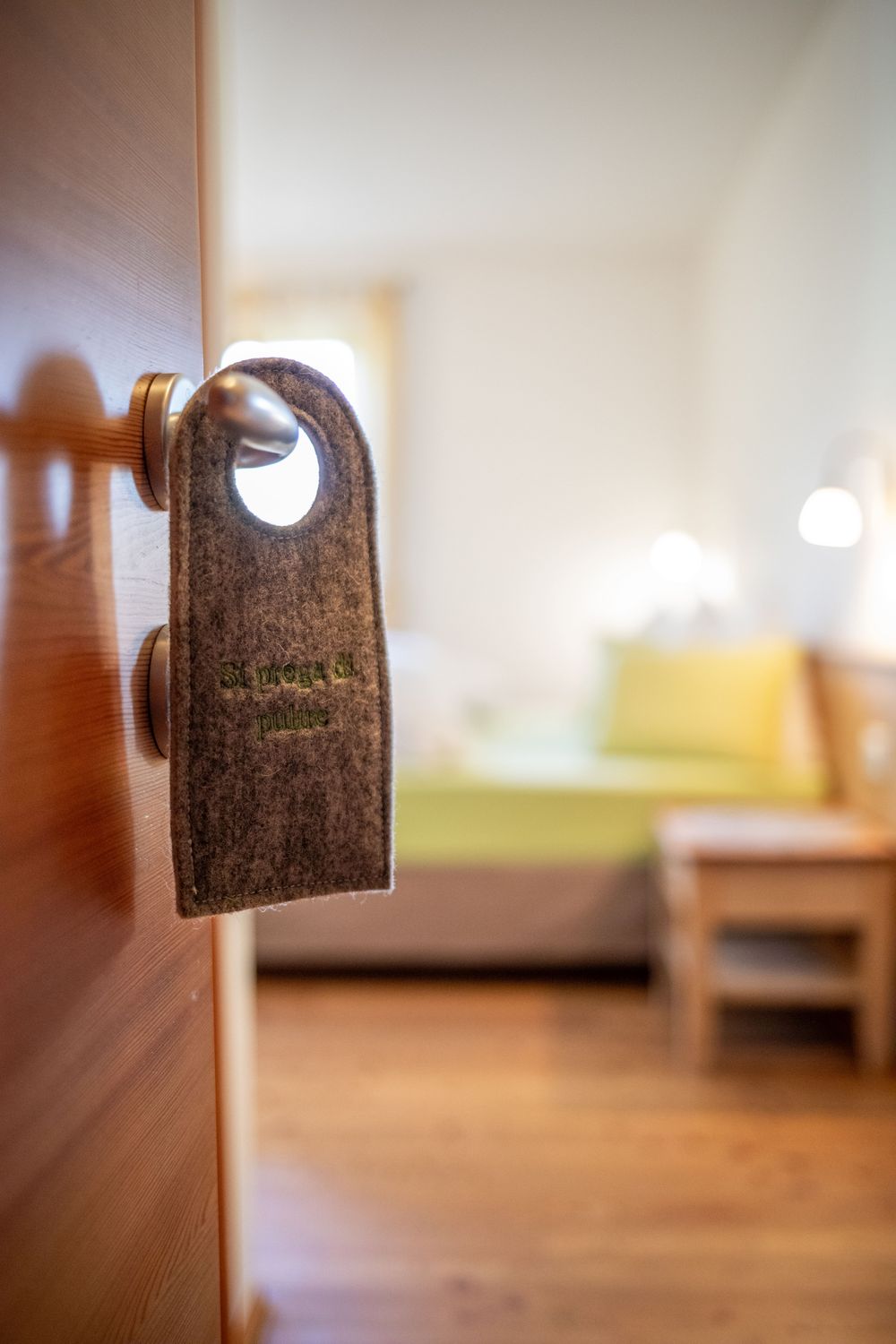 Ein Filz-Türanhänger mit der Aufschrift 'Si prega di pulire' an einer Hotelzimmertür.