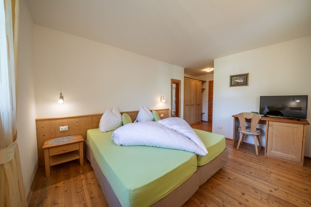 Ein gemütliches Hotelzimmer mit Doppelbett, hellem Holzmobiliar, Holzboden und Fernseher.